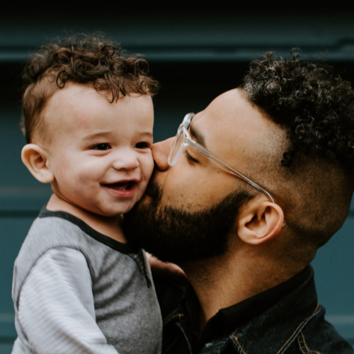 A man with glasses kisses a smiling child's cheek.
